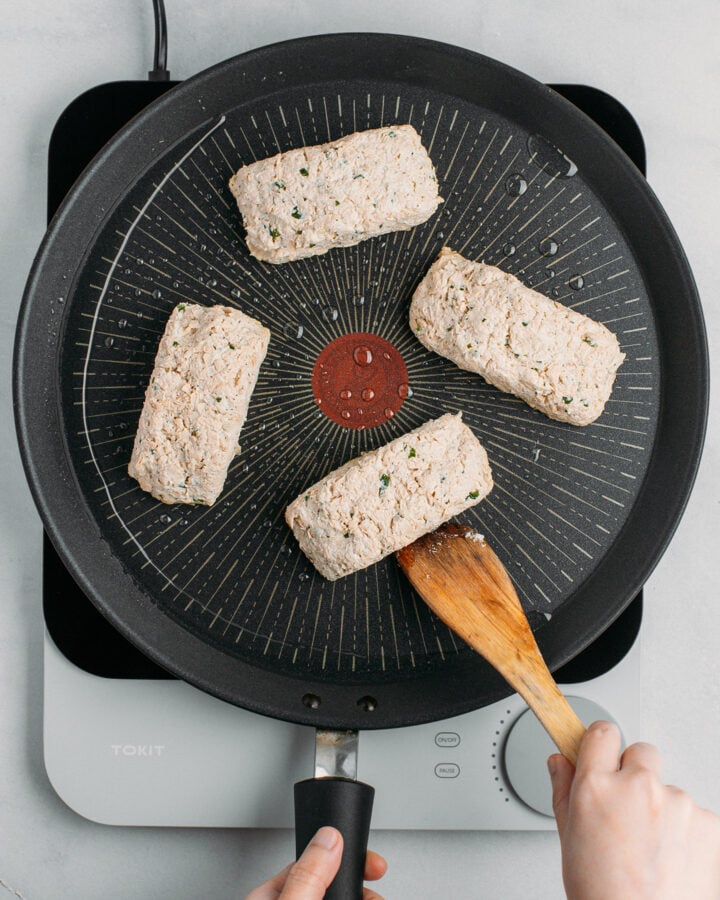 Four pieces of uncooked vegan fish on a non-stick skillet.