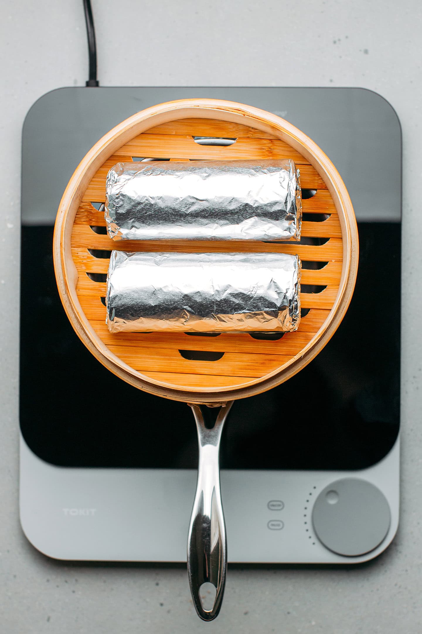 Two loaves of seitan wrapped in aluminum foil in a bamboo basket steamer.