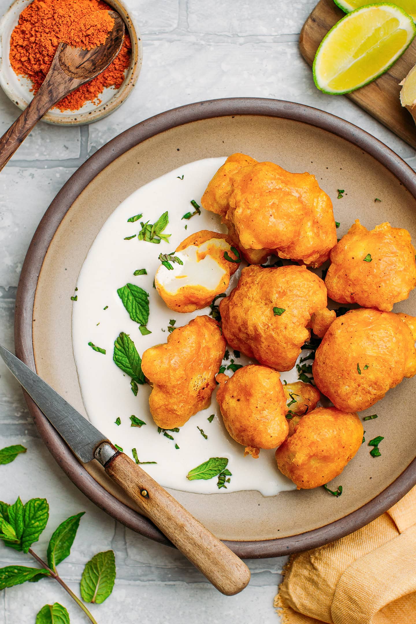 Cauliflower tempura with ginger sauce and mint leaves on a plate.