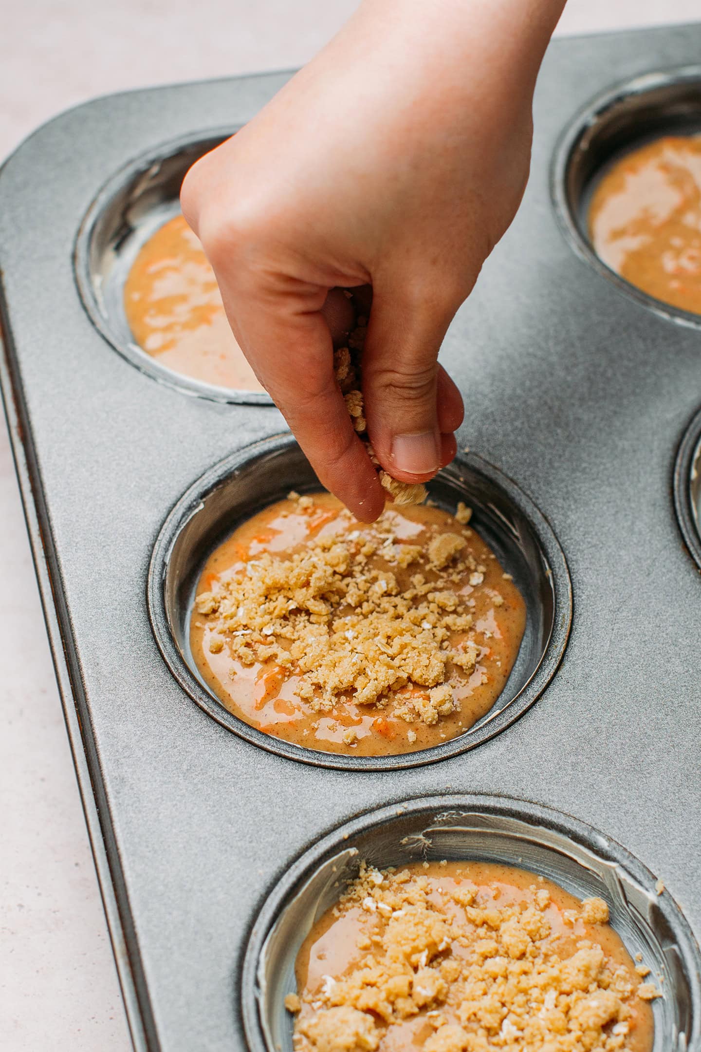 Sprinkling crumb topping on unbaked muffins.