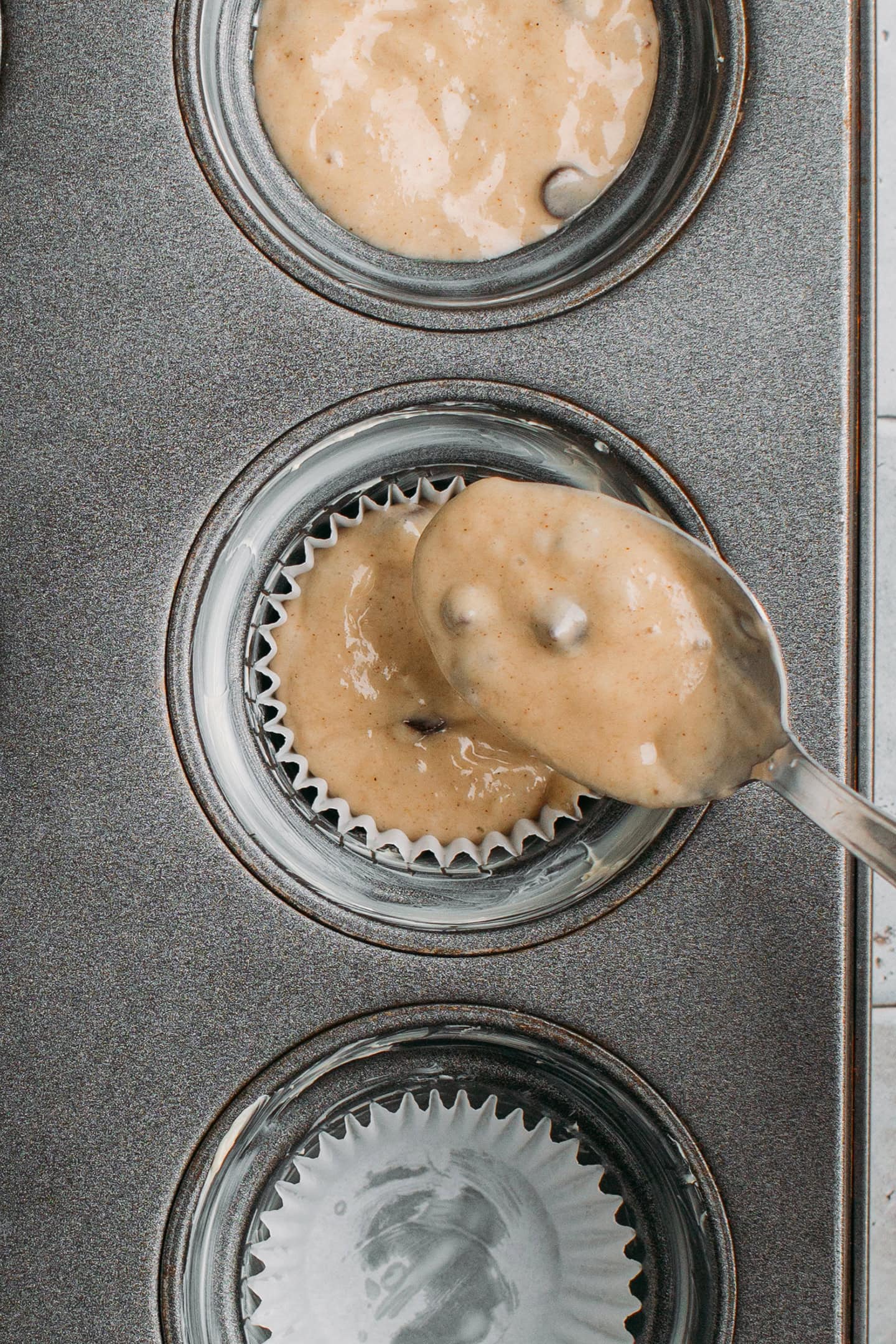 Pouring batter into a muffin cavity.