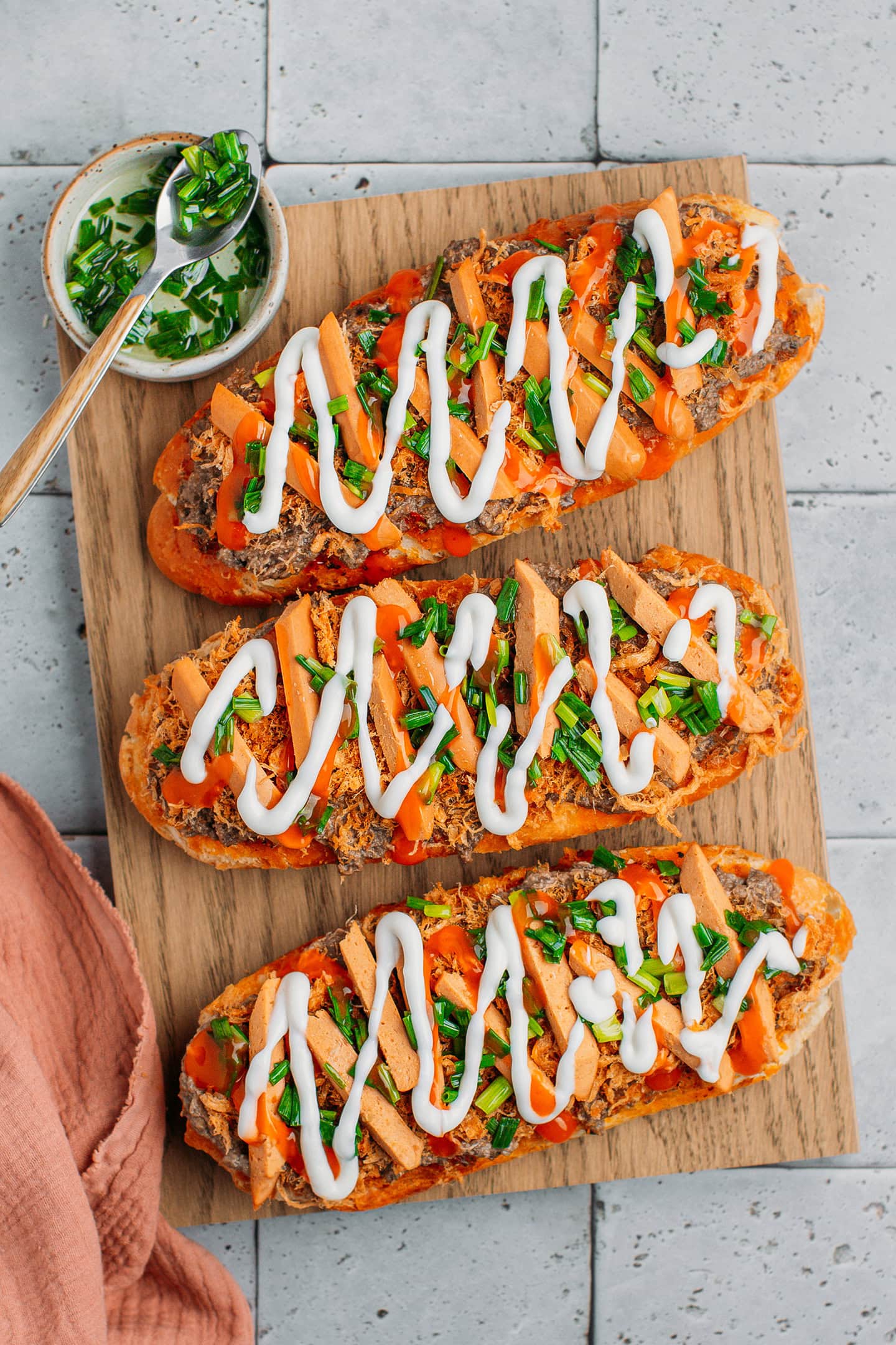 Three loaves of banh mi topped with pâté, sausages, green onions, and a drizzle of mayo and sweet chili sauce.