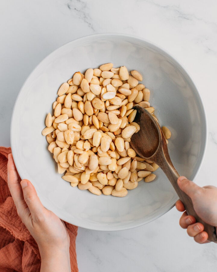 Tossing almonds with maple syrup, oil, and salt, in a bowl.