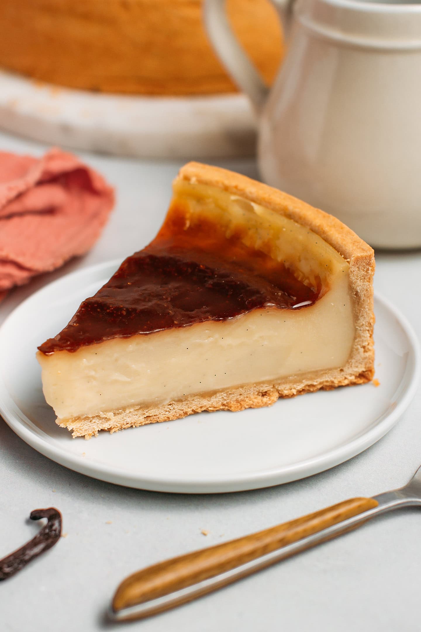 Slice of vegan custard tart with a creamy vanilla custard and a caramelized top, on a small white plate.