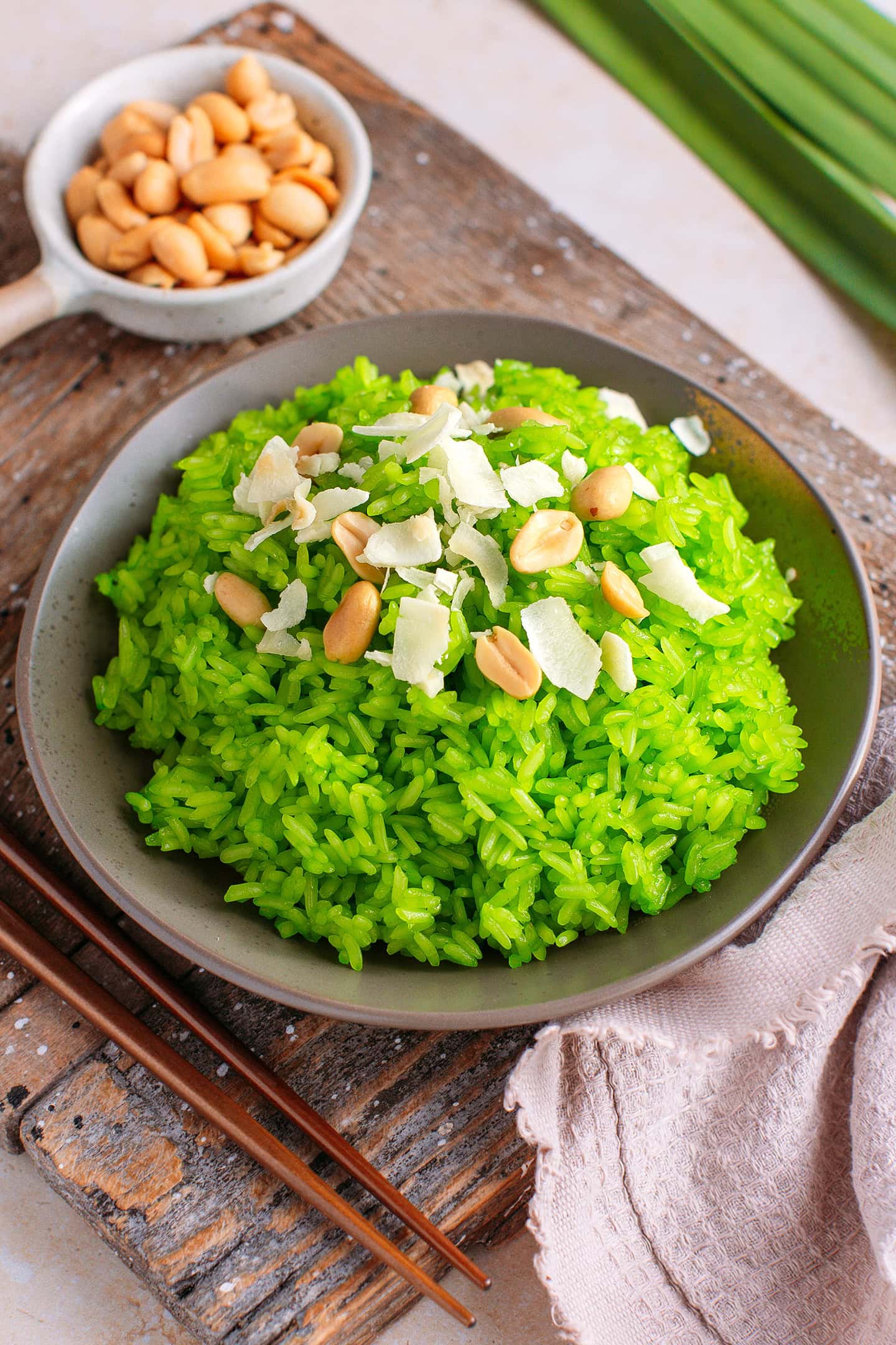 Pandan sticky rice on a small plate topped with roasted peanuts and coconut flakes.