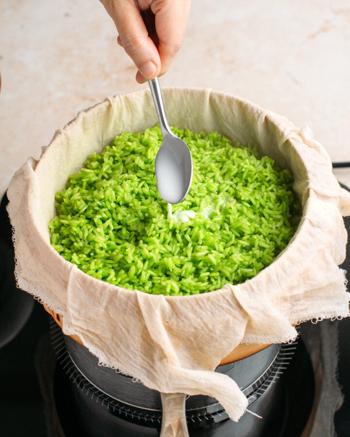Drizzling sweet coconut milk over pandan sticky rice in a steamer.