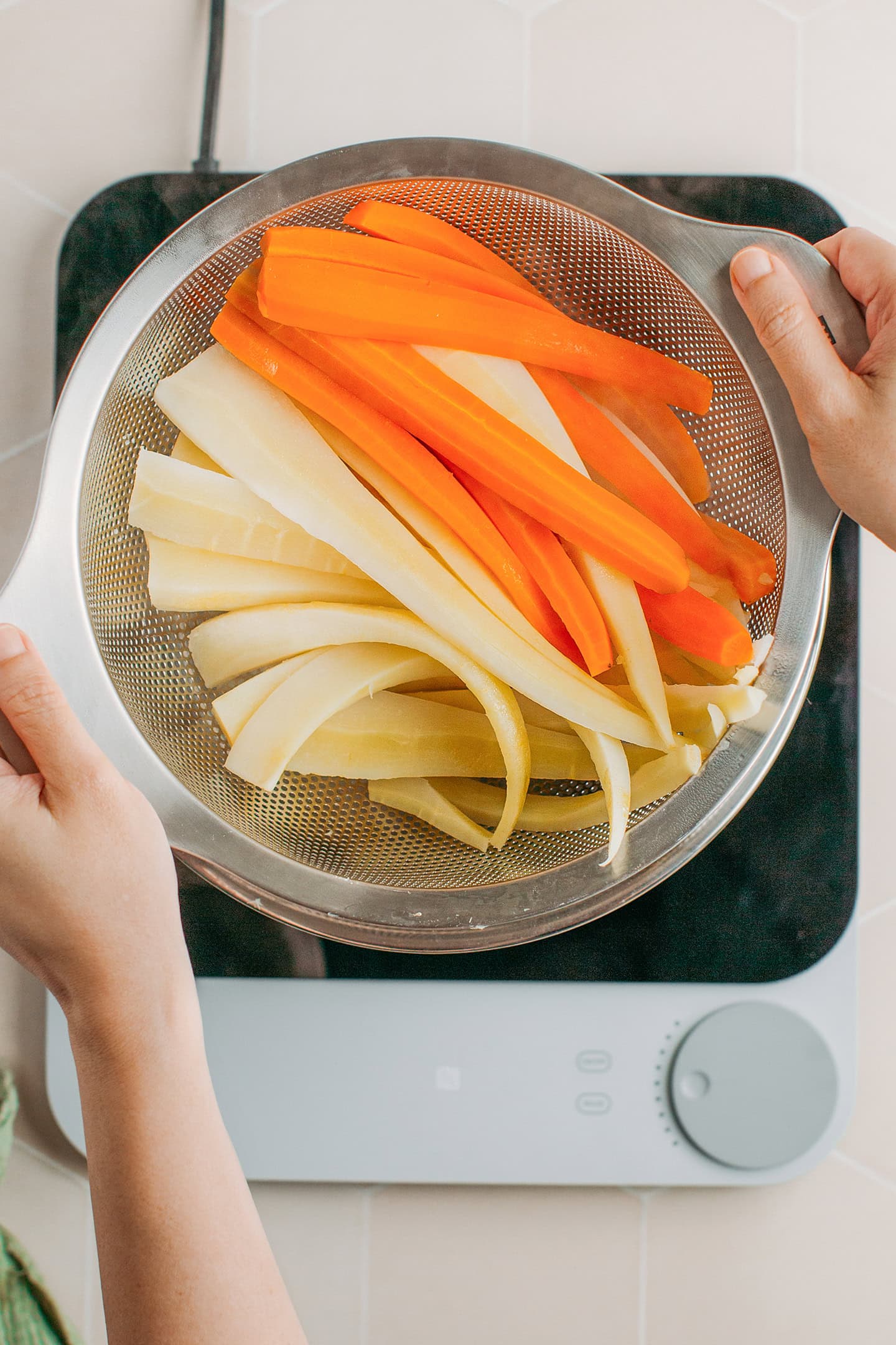 Draining cooked parsnips and carrots using a colander.
