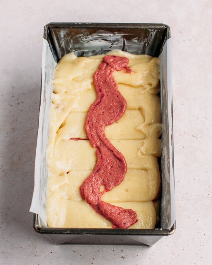 Swirl of strawberry batter on top of vanilla cake batter in a loaf pan.