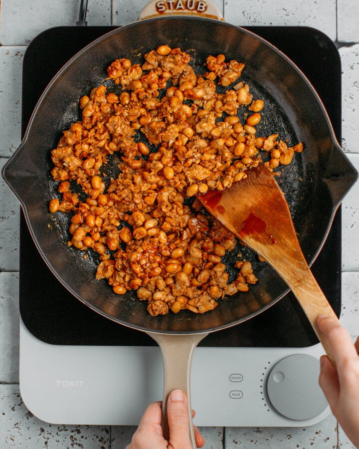 Stirring scrambled tofu with soy sauce in a skillet.
