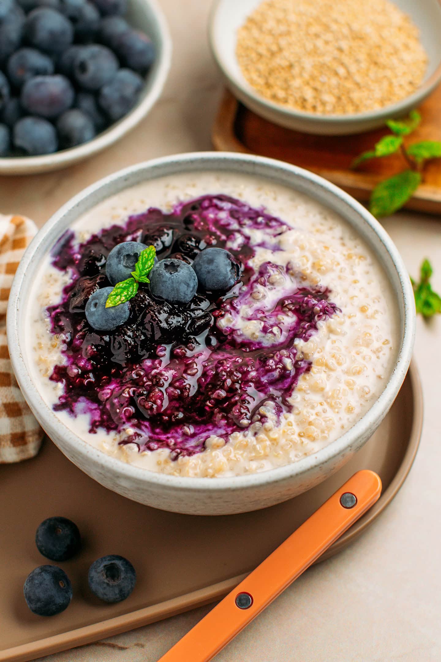 Ceramic bowl filled with quinoa pudding and topped with blueberry compote, fresh blueberries, and mint leaves.