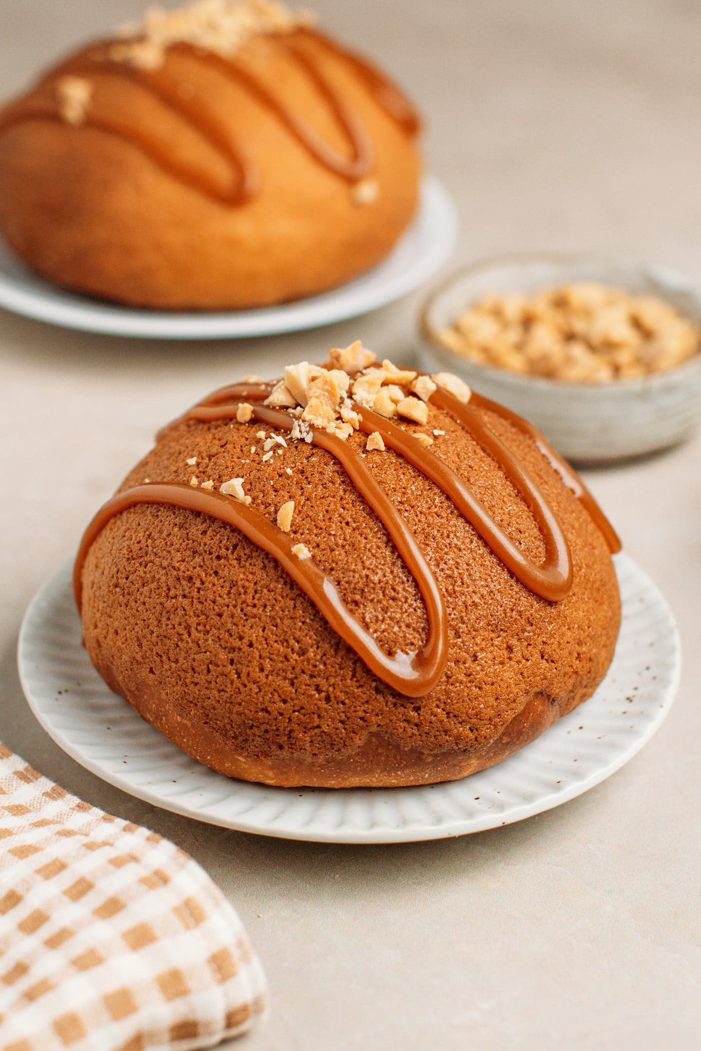 Coffee bun topped with caramel sauce and peanuts on a small plate.