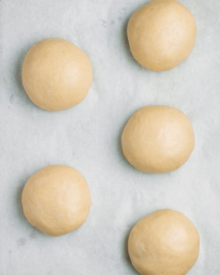 Five balls of dough, after rising, on a baking sheet.