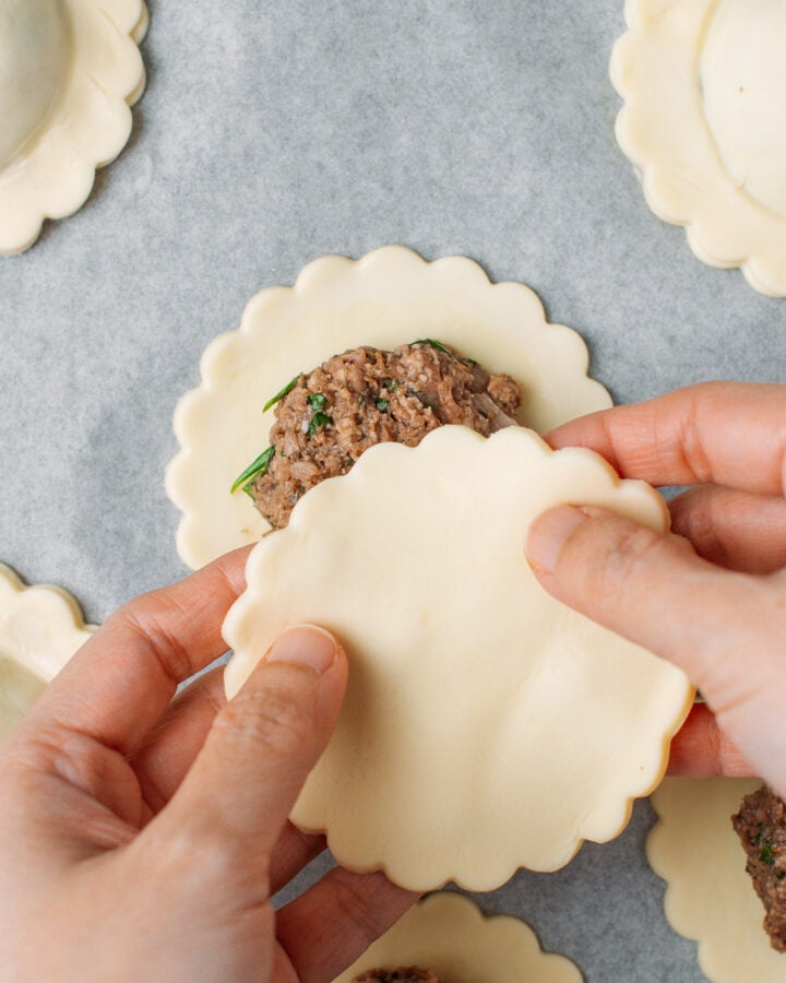 Placing another round of puff pastry over a vegan meat filling.