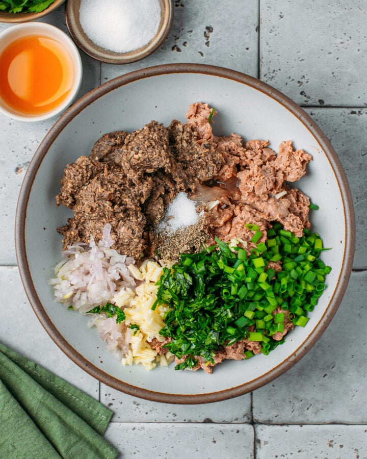 Vegan ground meat, pâté, chopped green onions, garlic, and shallot in a mixing bowl.