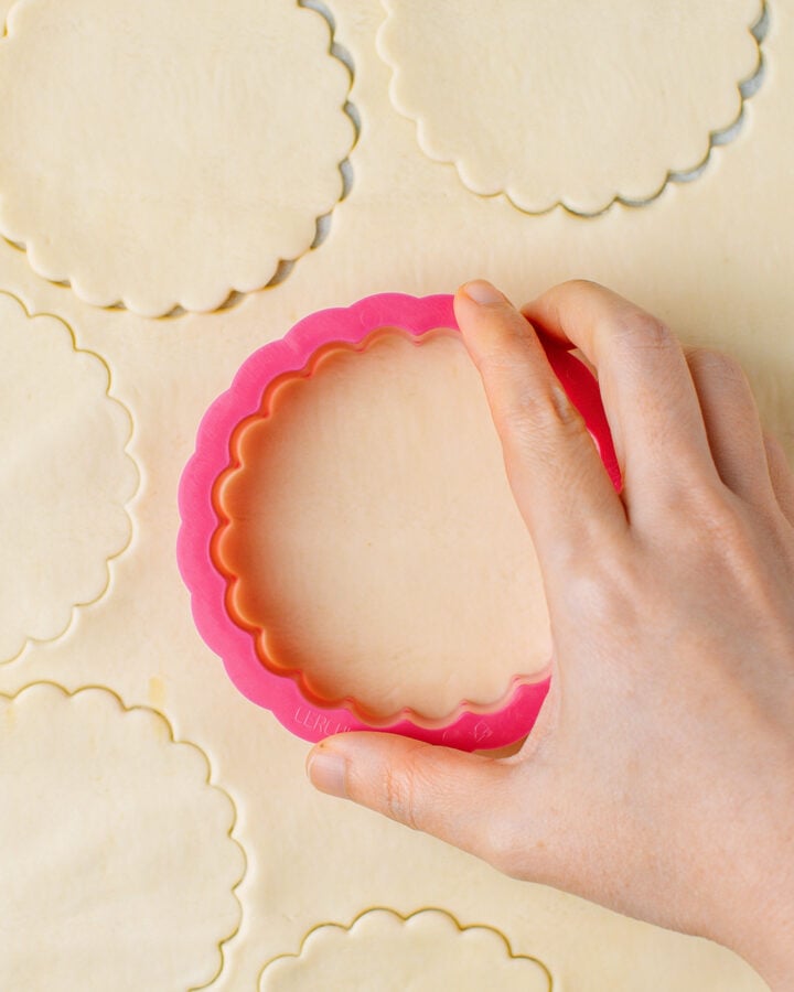 Cutting out a round of puff pastry using a cookie cutter.