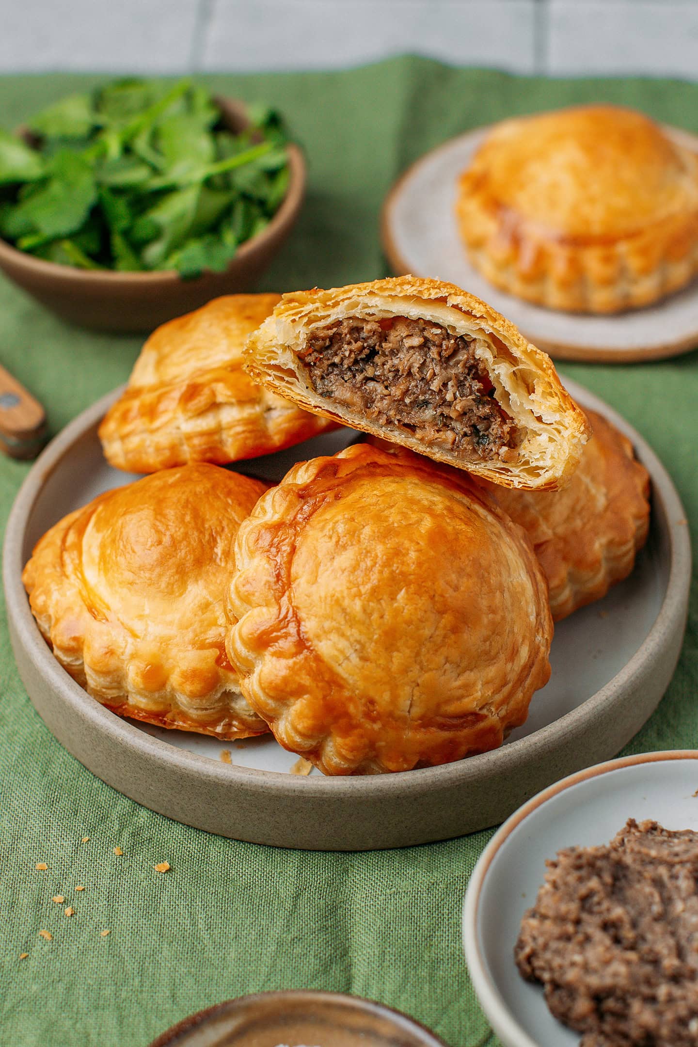 Five vegan meat pastries on a small plate placed on a green tablecloth.
