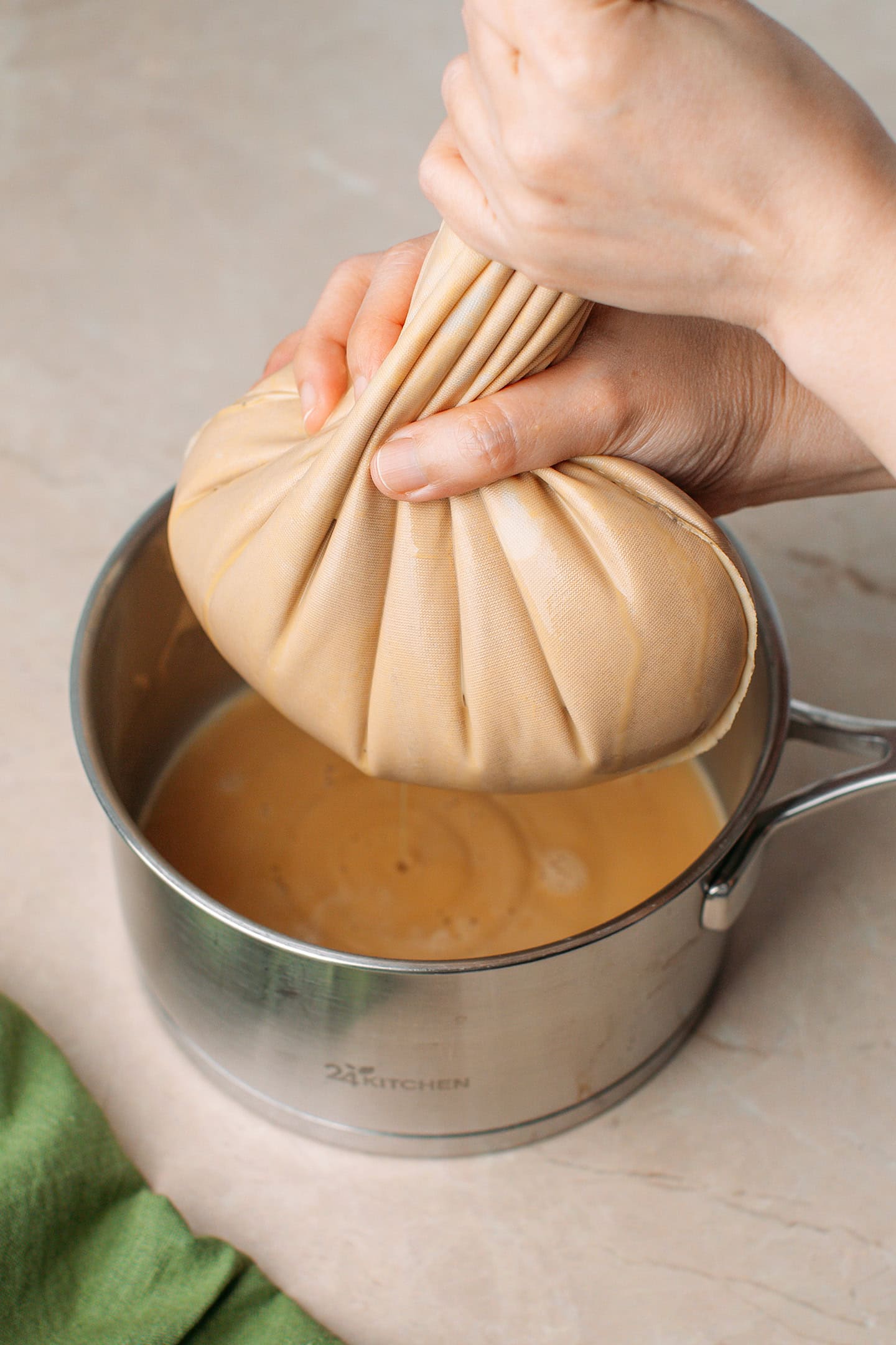 Squeezing a nut milk bag over a saucepan.