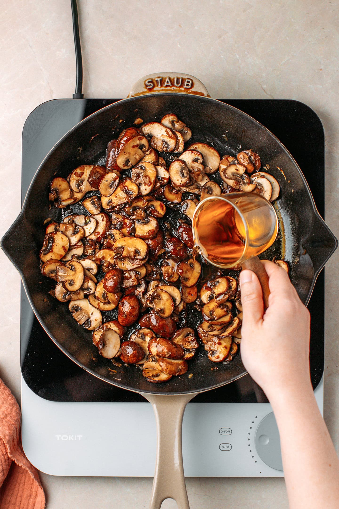 Pouring white wine into a skillet containing sautéed mushrooms.