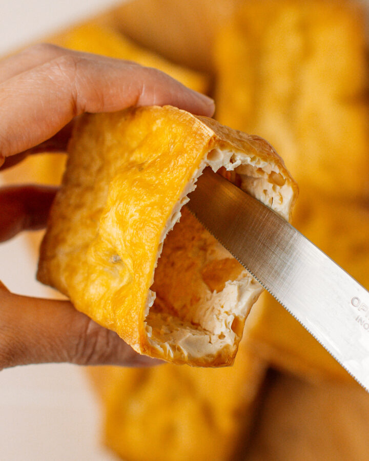 Using a knife to remove the inside from a piece of fried tofu.