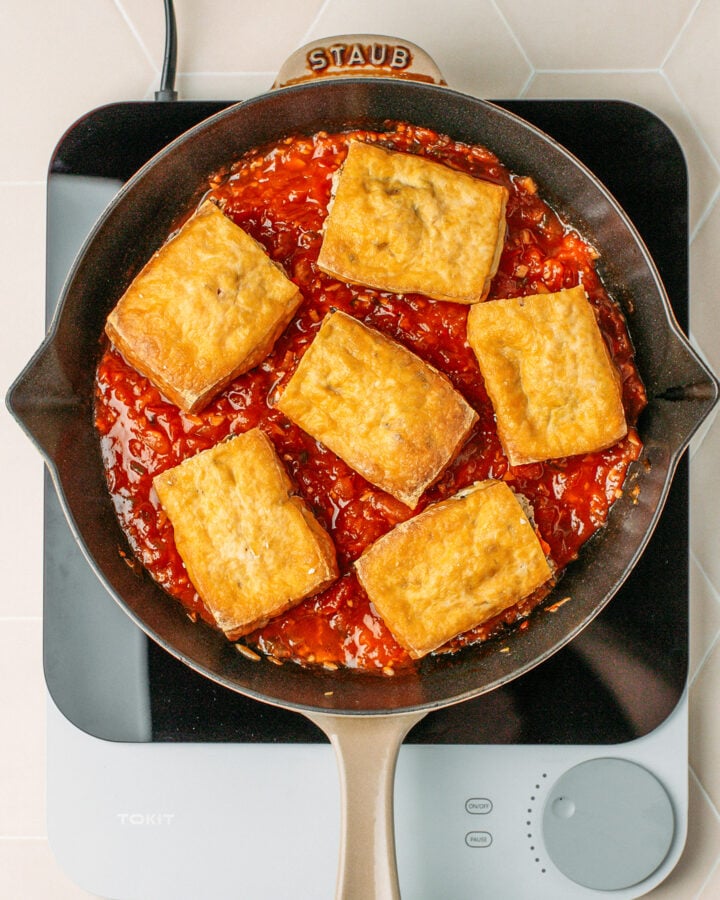 Six pieces of stuffed tofu in tomato sauce in a skillet.