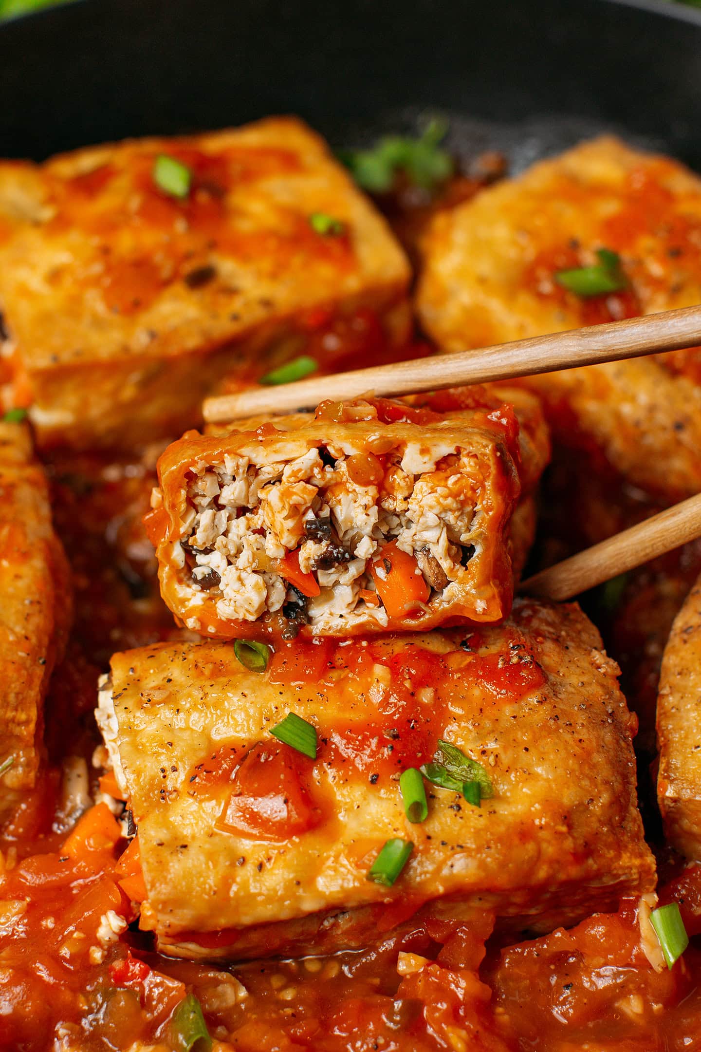 Holding a piece of stuffed tofu using chopsticks.