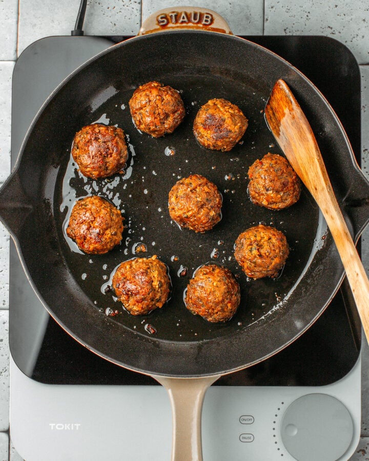 Nine sautéed vegan meatballs in a skillet.