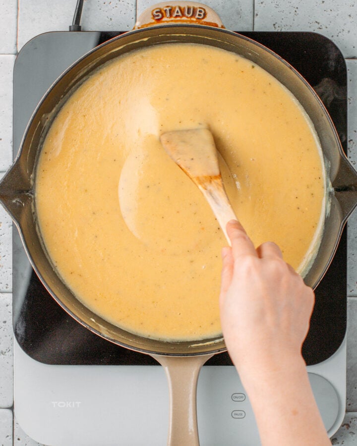 Using a spatula to mix vegan cream, vegetable broth, and butter in a skillet.