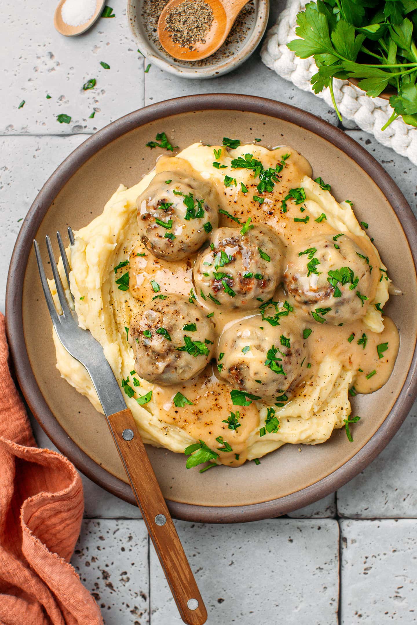 Five vegan meatballs with a gravy over mashed potatoes in a brown plate.