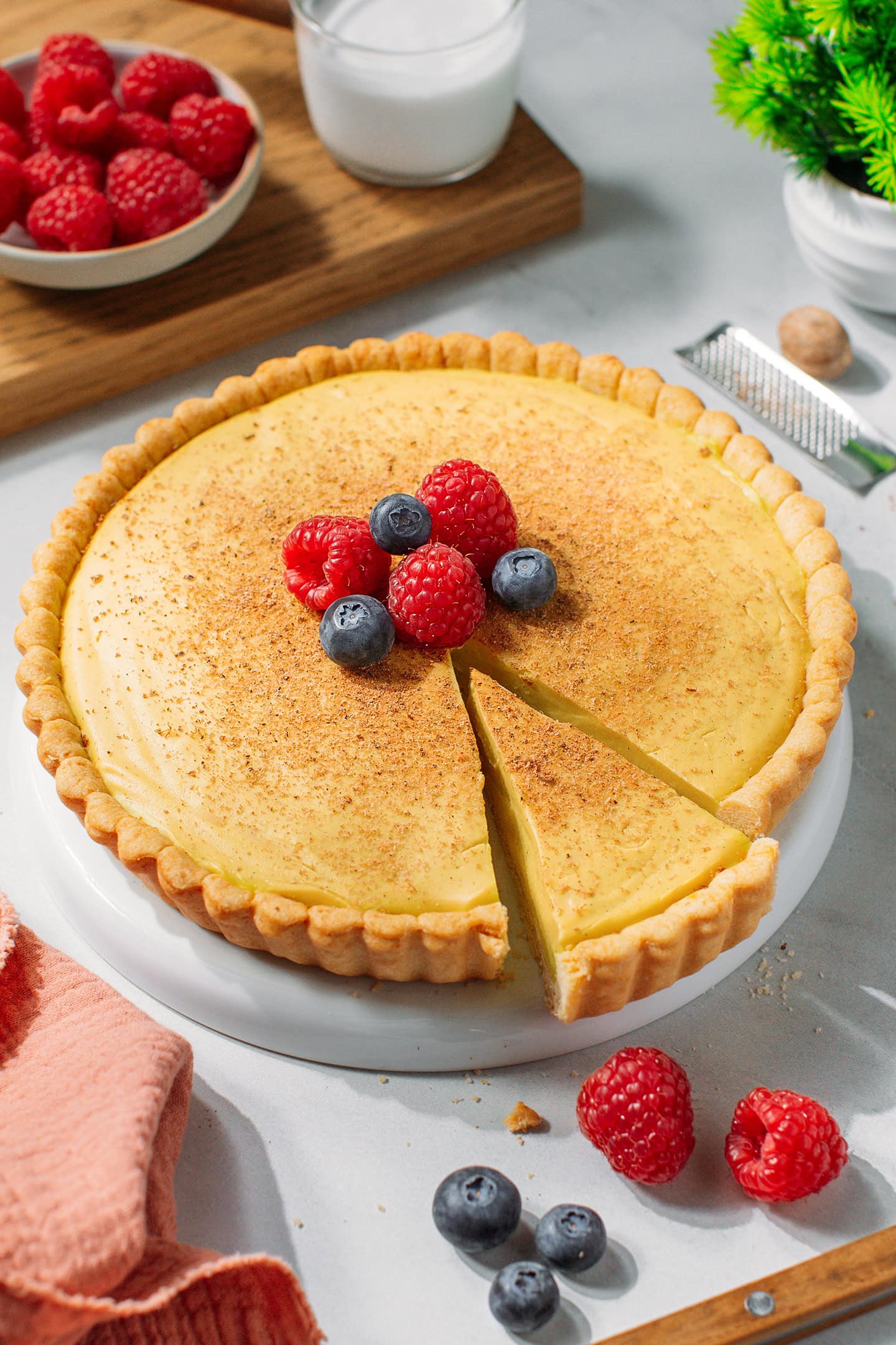 Sliced custard tart topped with fresh raspberries and blueberries on a plate.