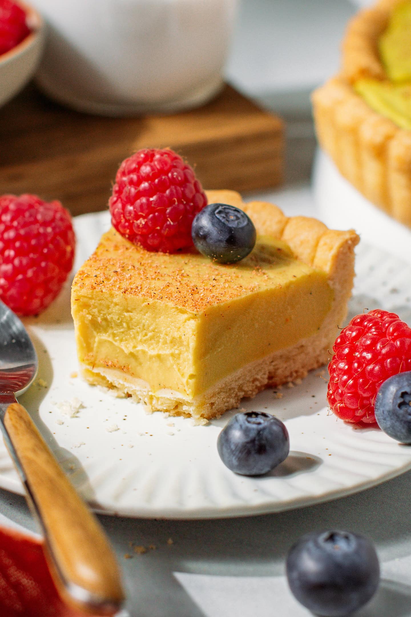 Slice of custard tart topped with raspberries and blueberries.