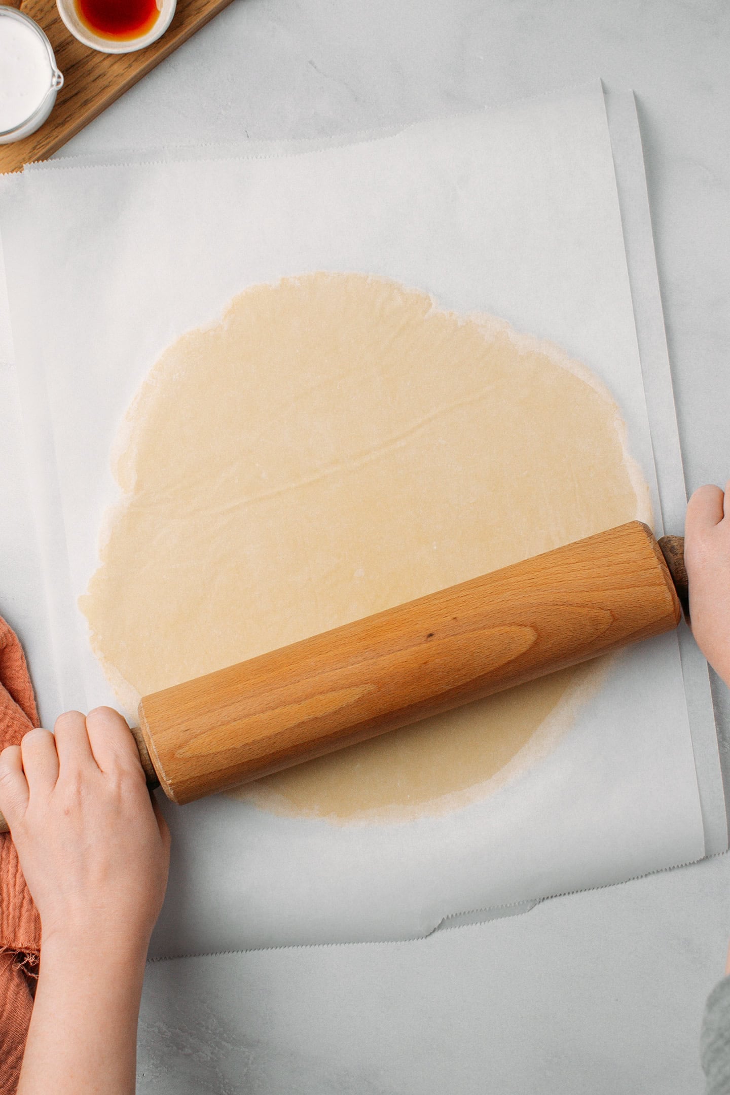 Using a rolling pin to flatten a dough between two layers of parchment paper.