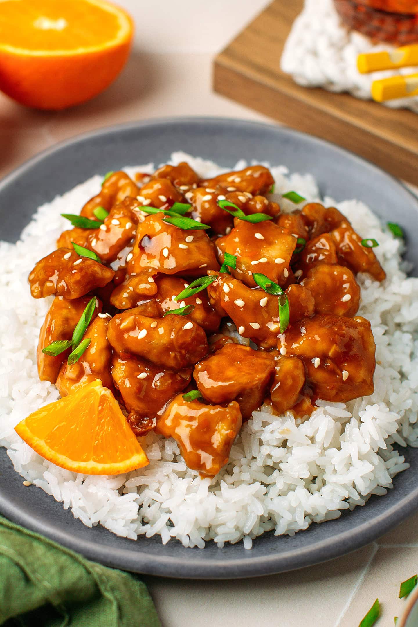 Close-up of a plate filled with white rice, orange tofu, sesame seeds, and chopped green onions.