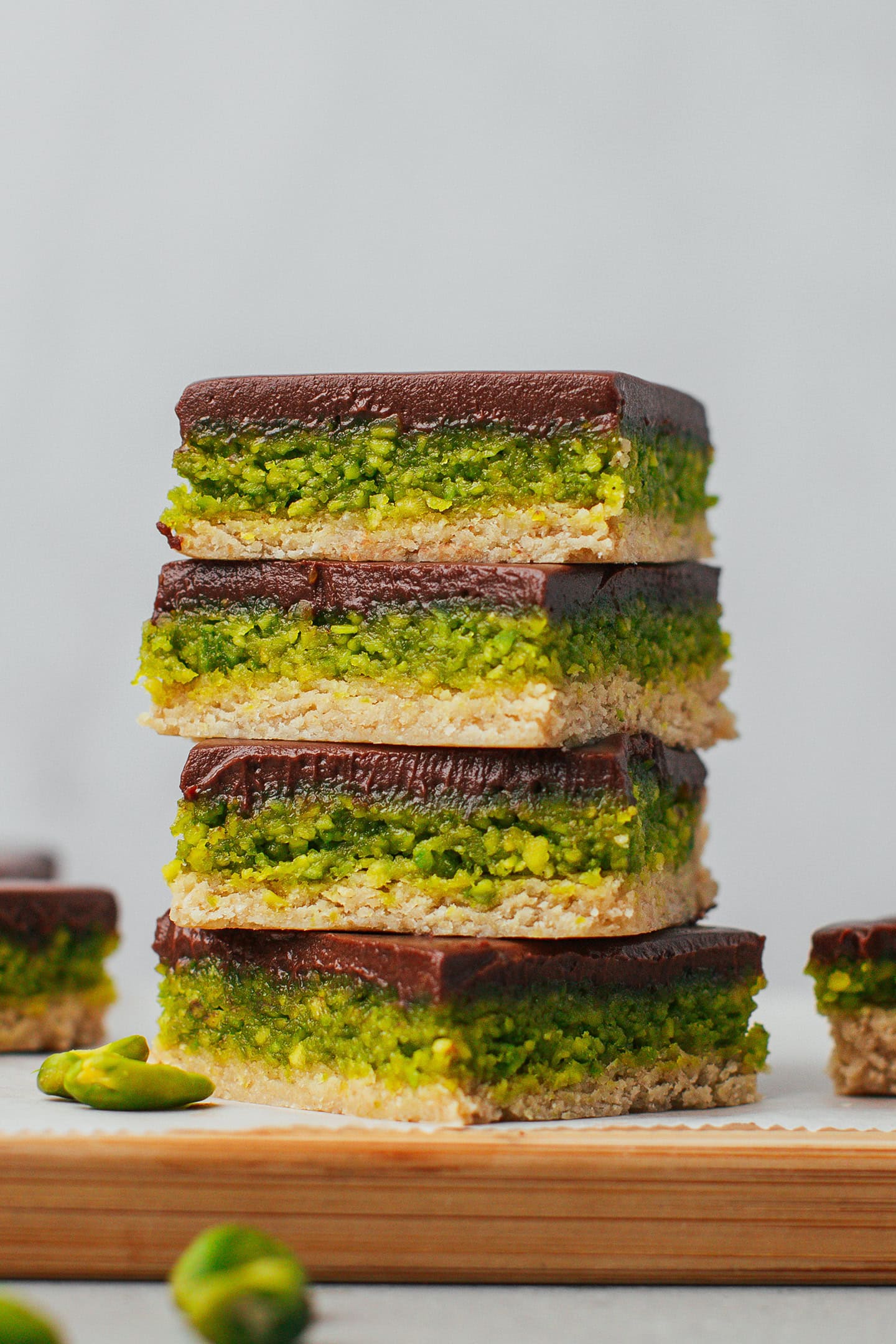 Four no-bake pistachio bars with chocolate ganache stacked.