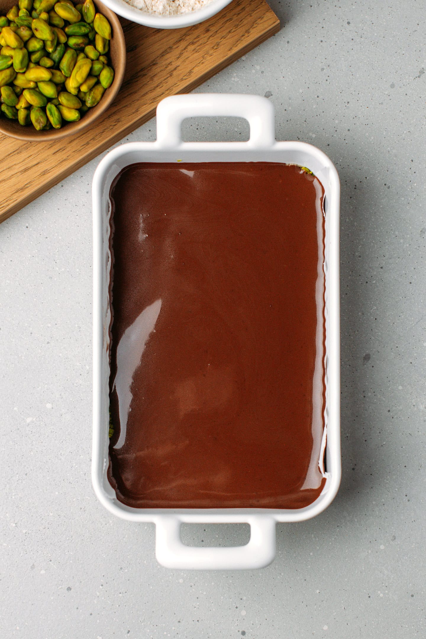 Baking dish filled with a layer of shortbread, pistachio meal, and chocolate ganache.