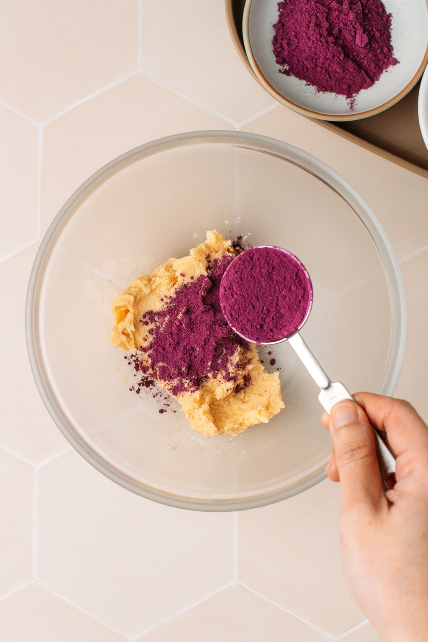 Adding ube powder to a bowl containing creamed butter.