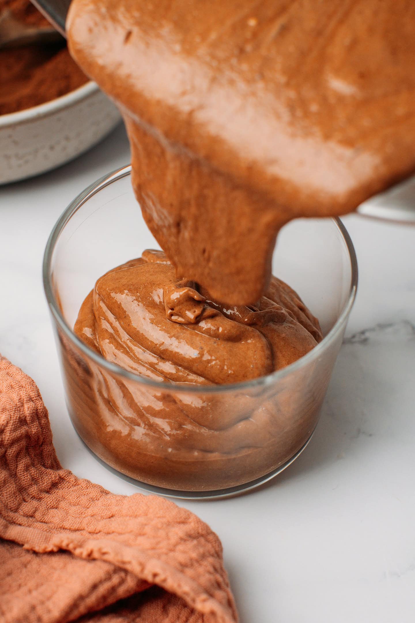 Pouring chocolate hazelnut mousse into a glass ramekin.