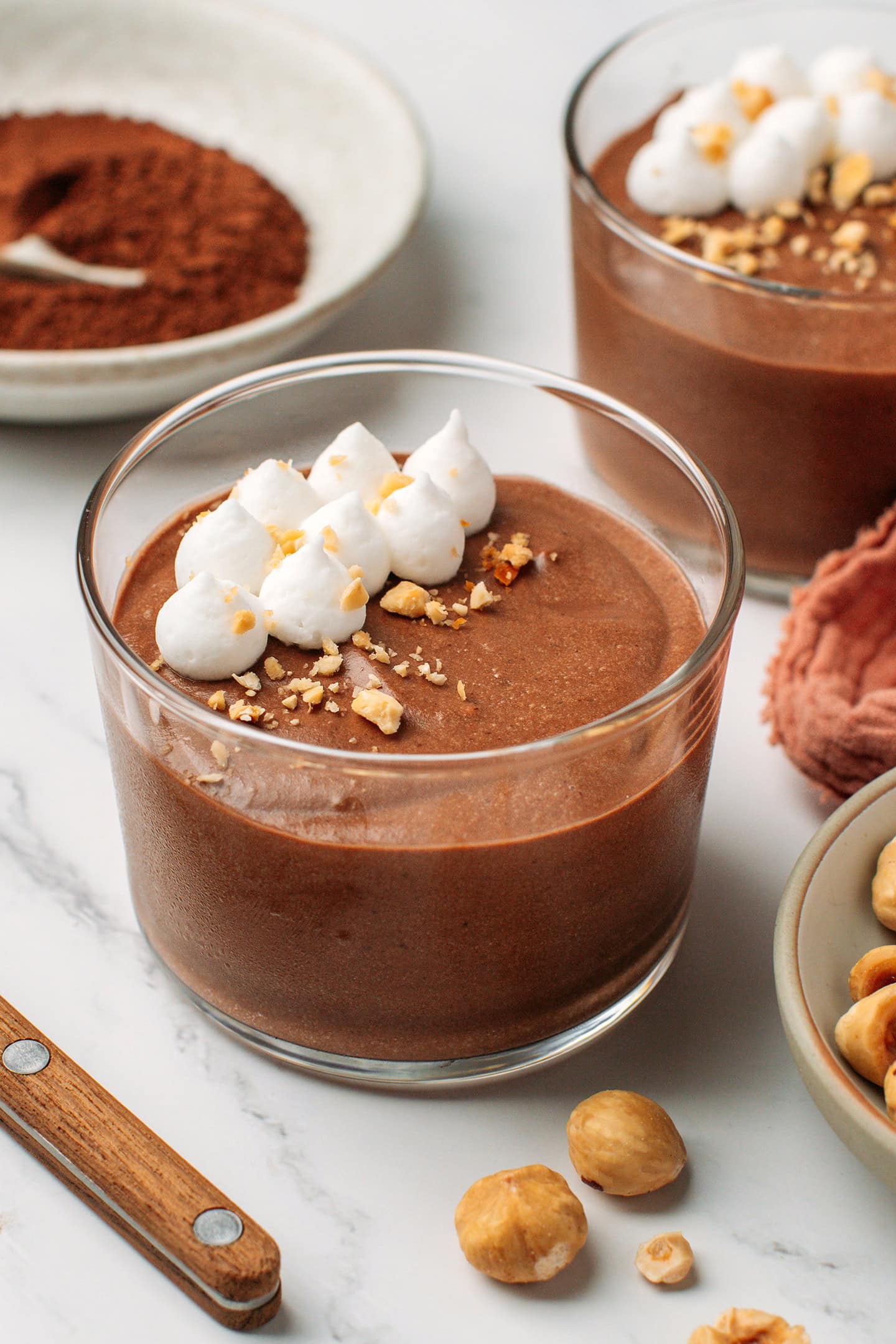 Glass ramekin filled with chocolate hazelnut mousse and topped with vegan whipping cream.
