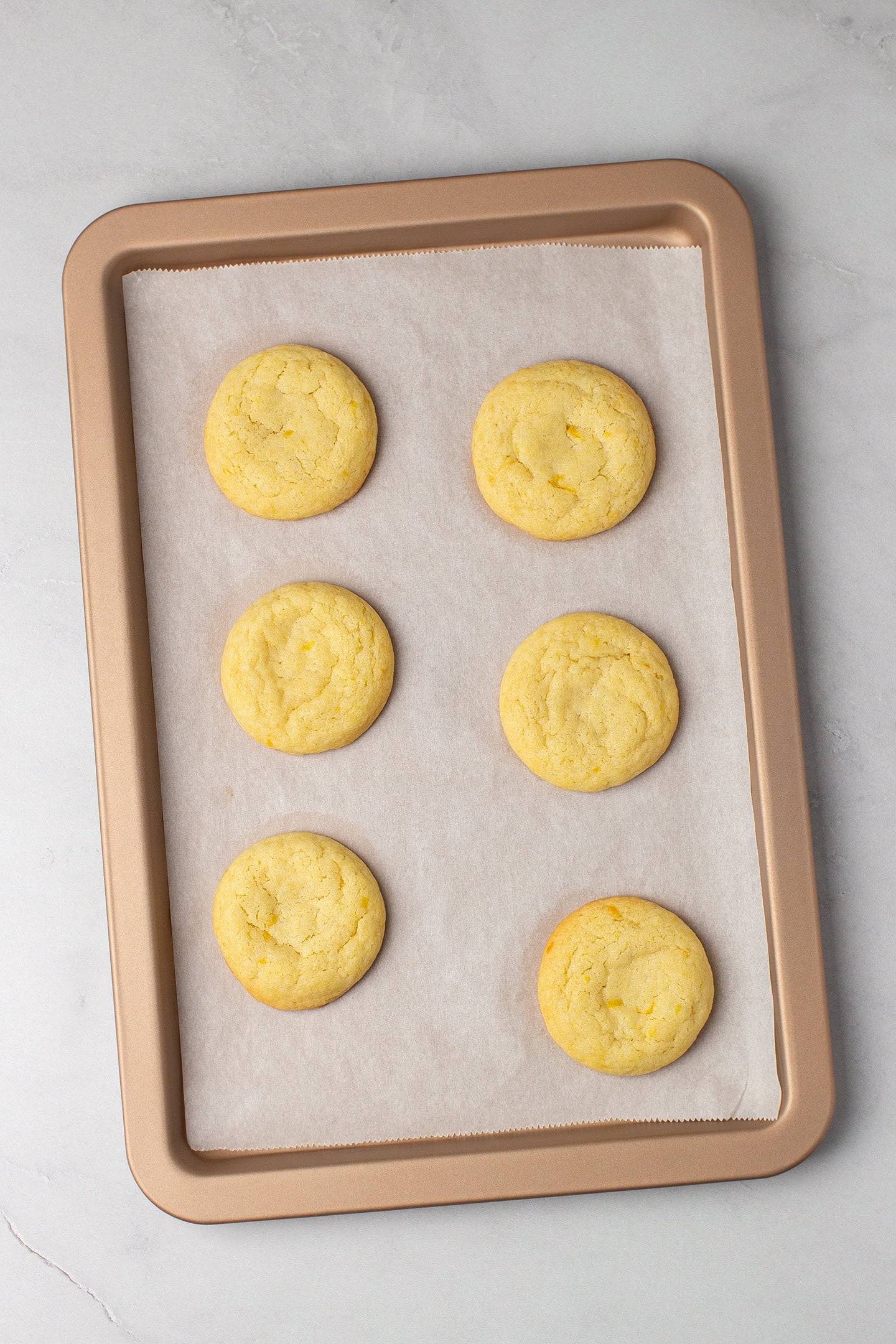 Six baked lemon cookies on a baking sheet.
