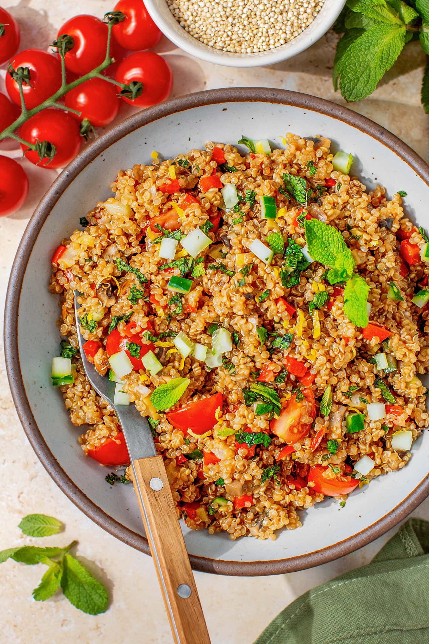 Fresh quinoa salad with diced cucumber, cherry tomatoes, and mint leaves in a bowl.