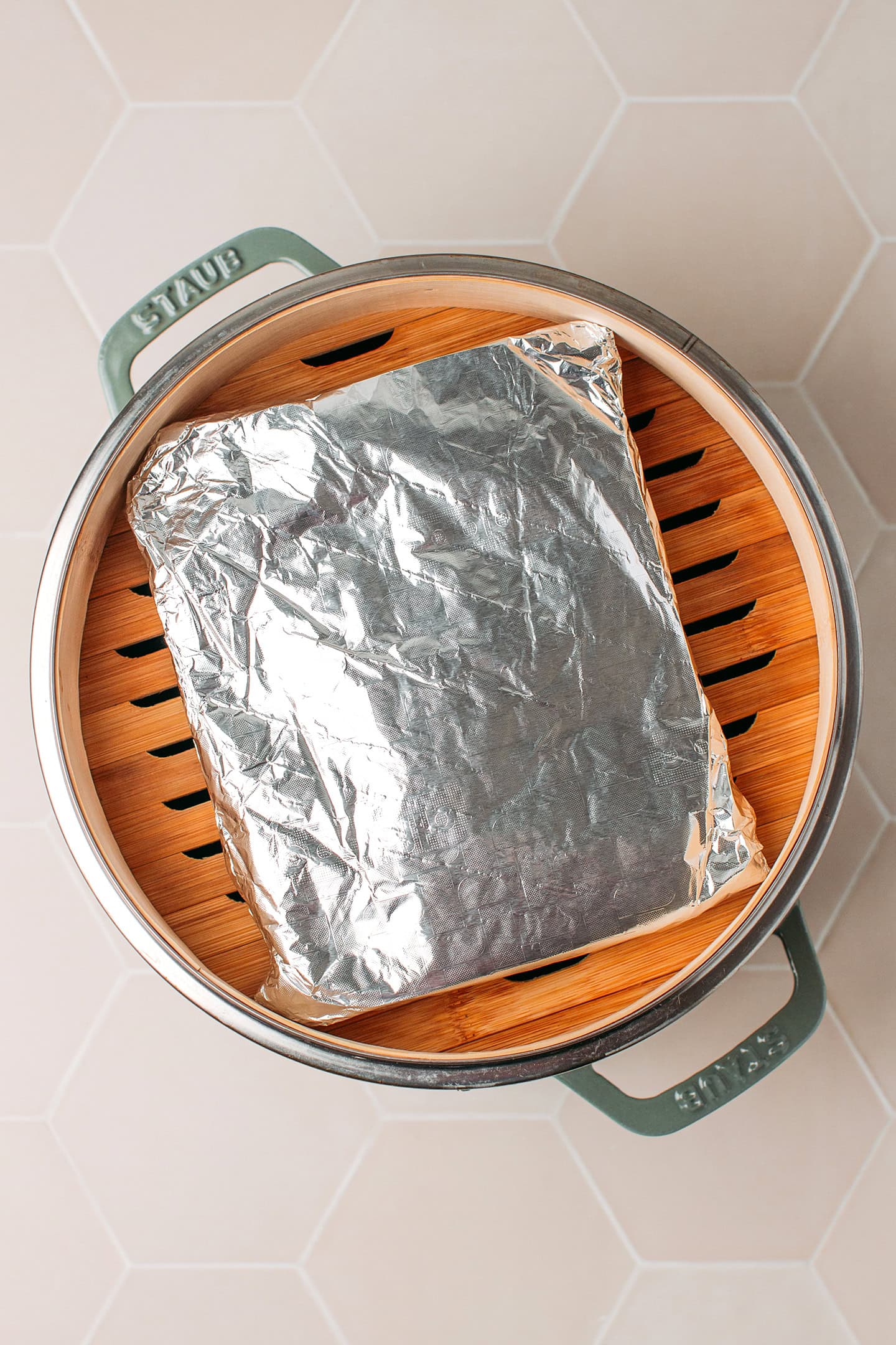 Loaf of seitan wrapped in aluminum foil in a steamer basket.