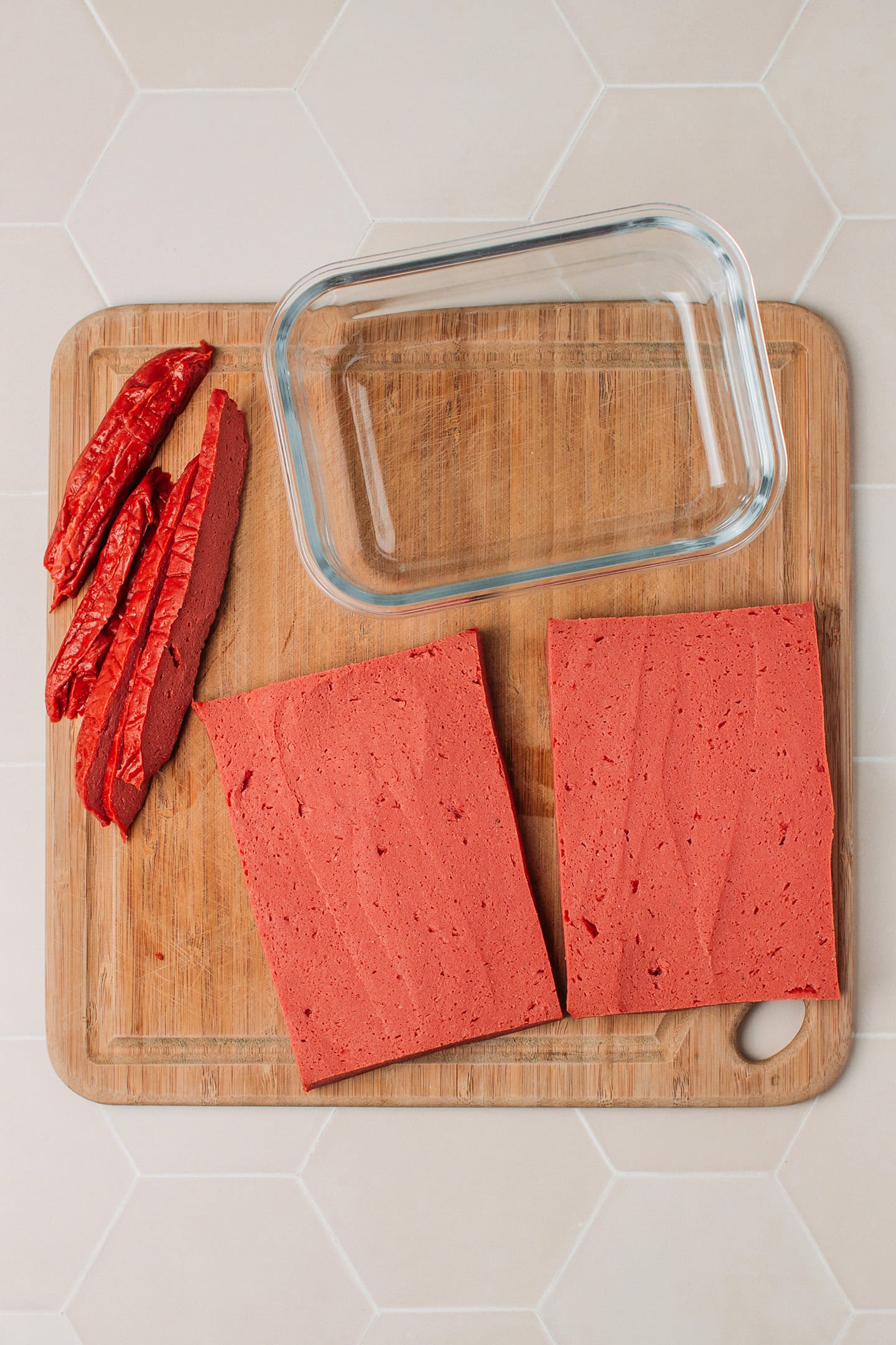 Two rectangles of seitan and a baking dish on a wooden board.