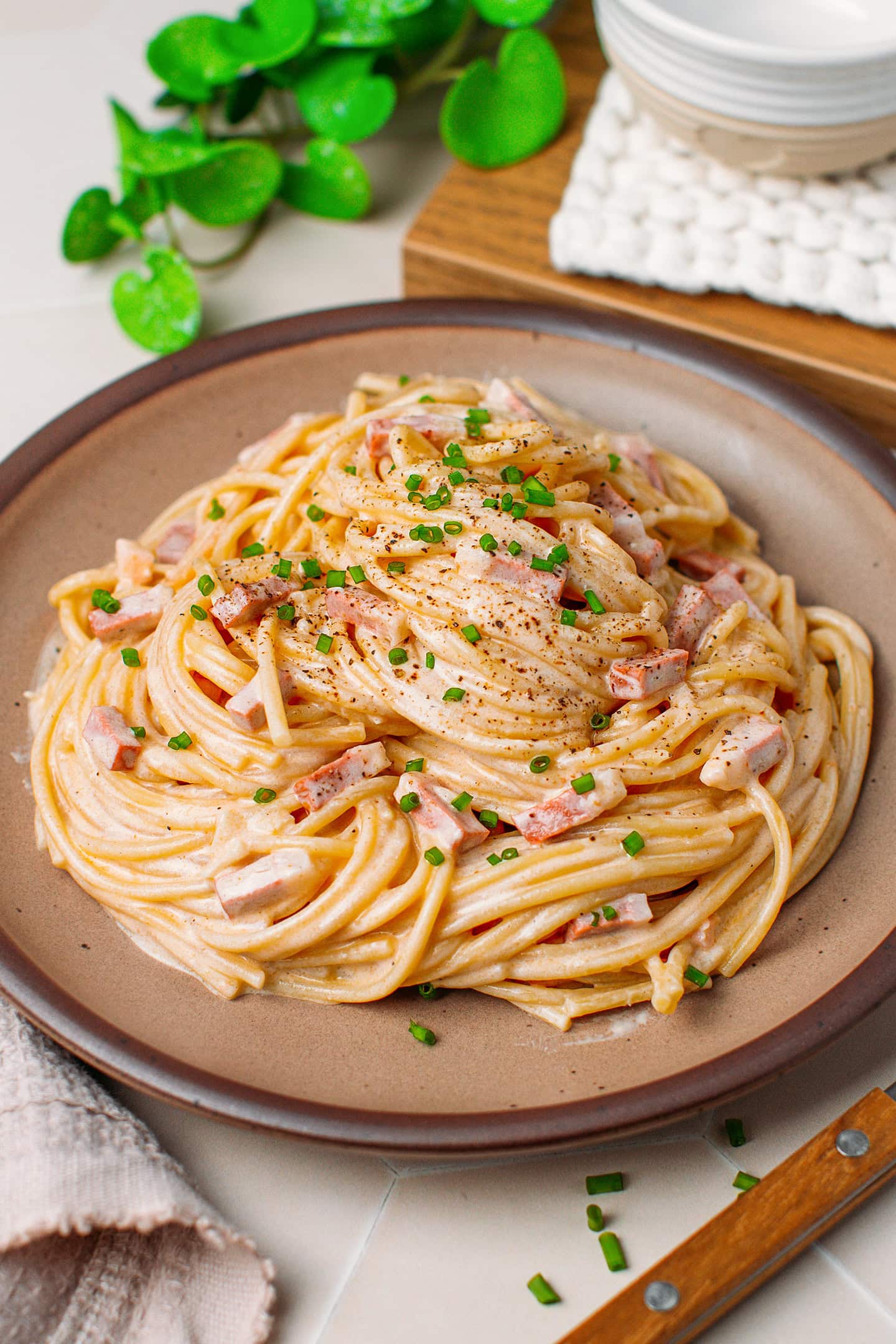 Vegan carbonara with ground black pepper and chives in a brown plate.