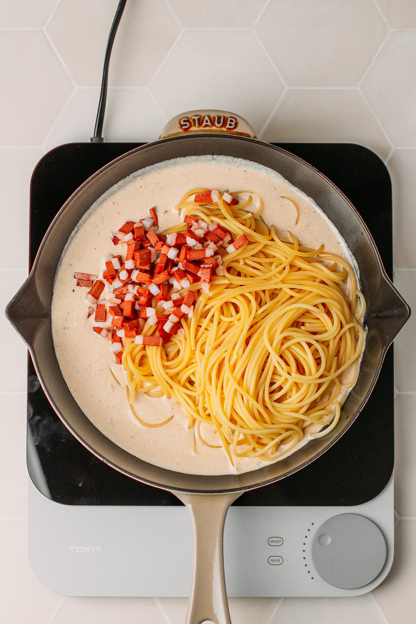 Vegan carbonara sauce, cooked spaghetti, and vegan bacon bits in a skillet.
