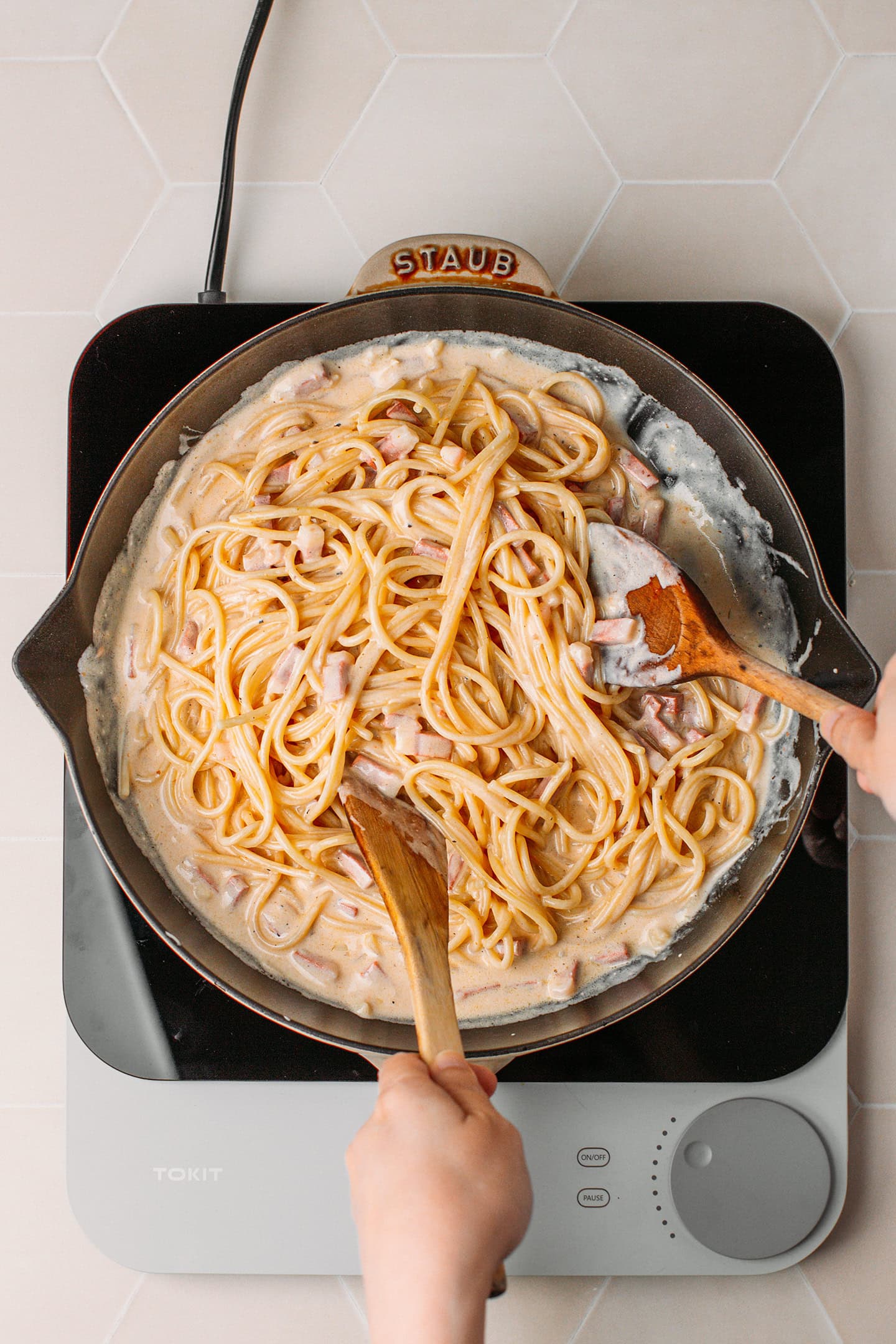 Tossing spaghetti with carbonara sauce and vegan bacon bits.
