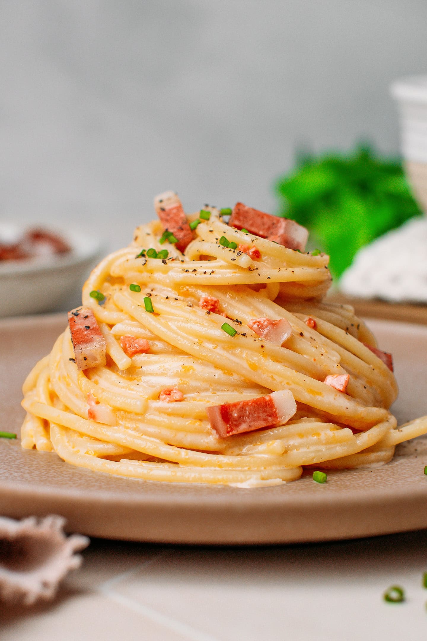 Nest of vegan carbonara pasta with bacon bits, ground black pepper, and chopped chives.