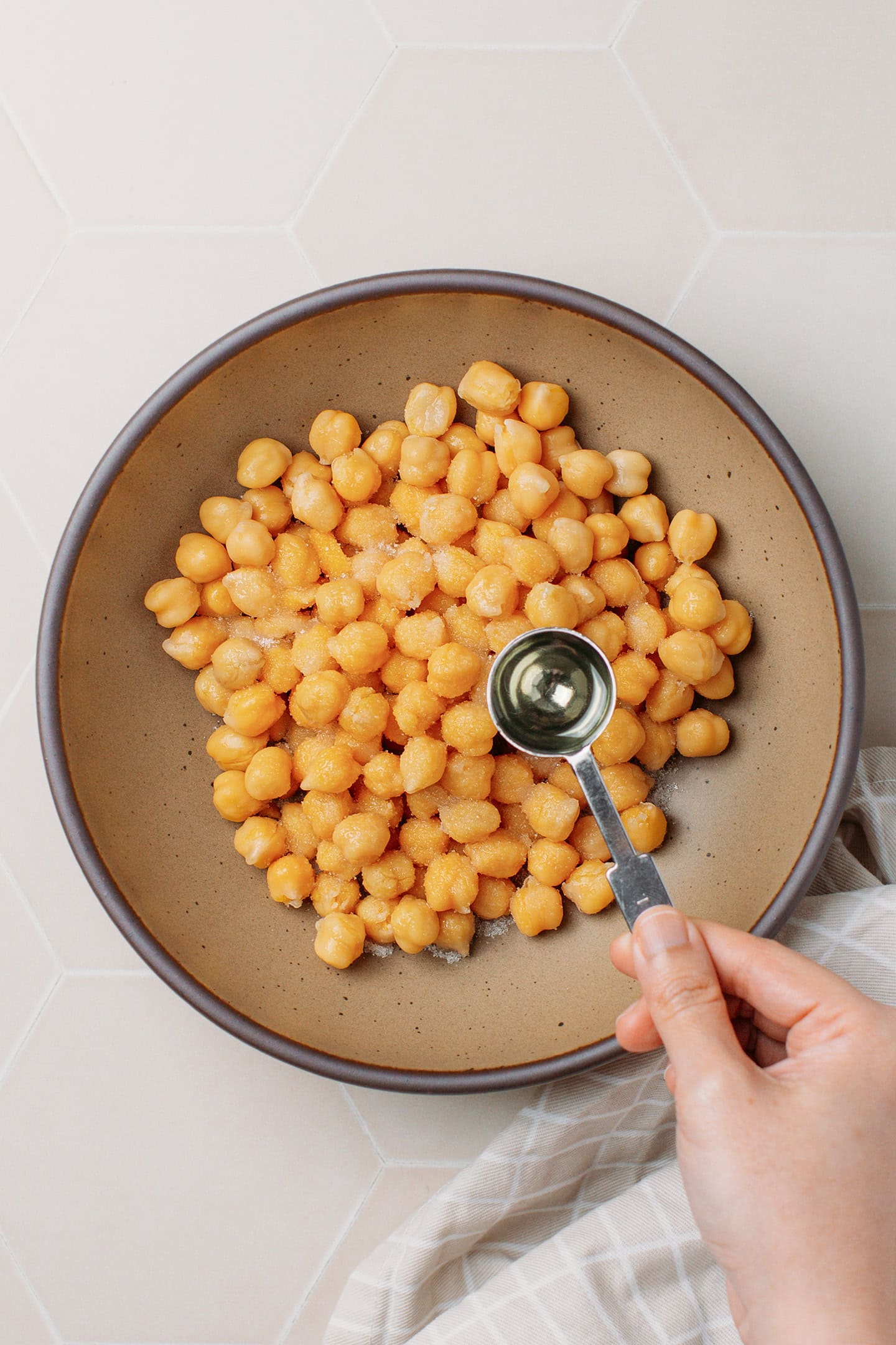 Pouring a teaspoon of oil inside a bowl containing cooked chickpeas.