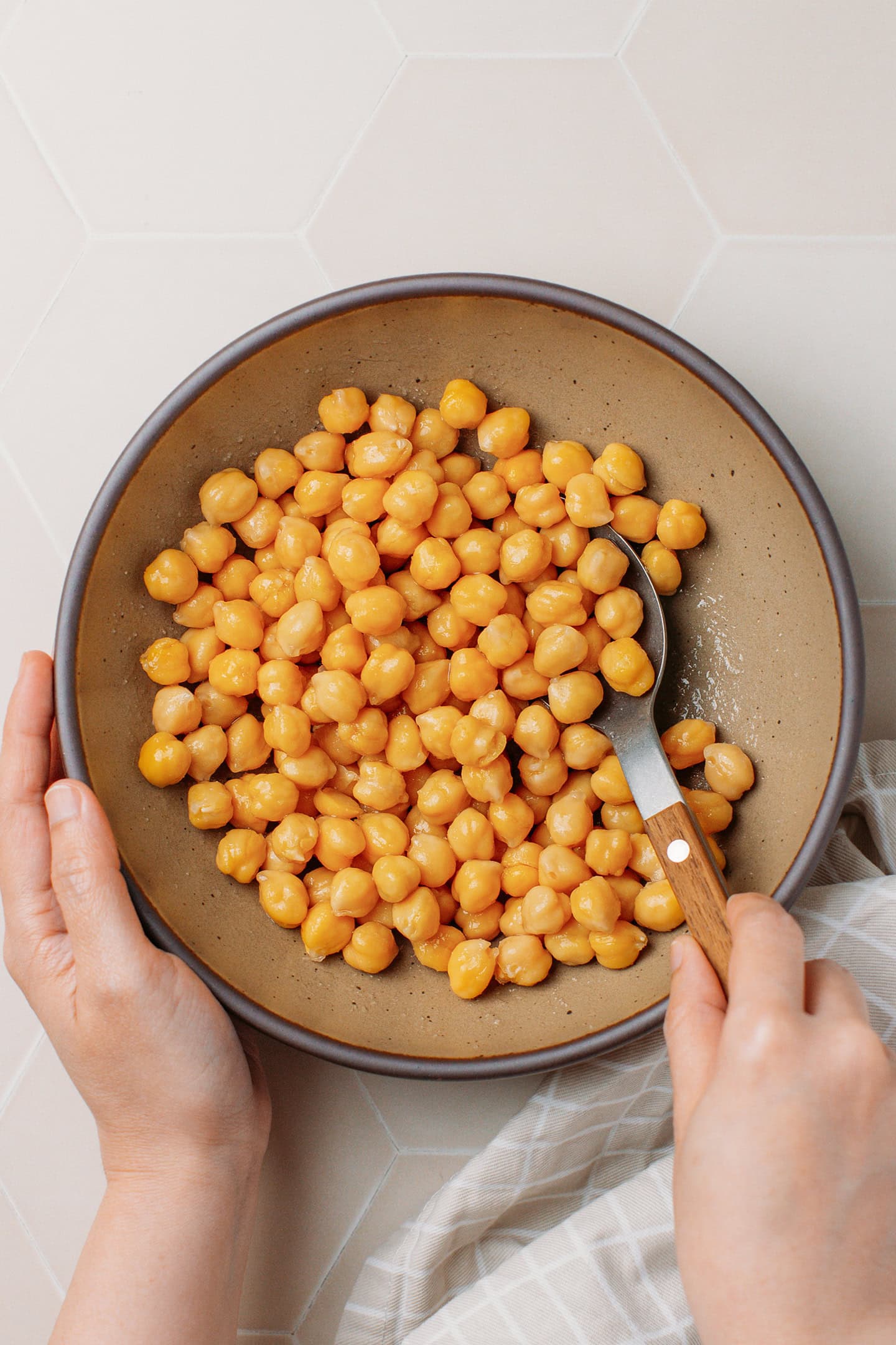 Tossing cooked chickpeas with oil in a bowl.