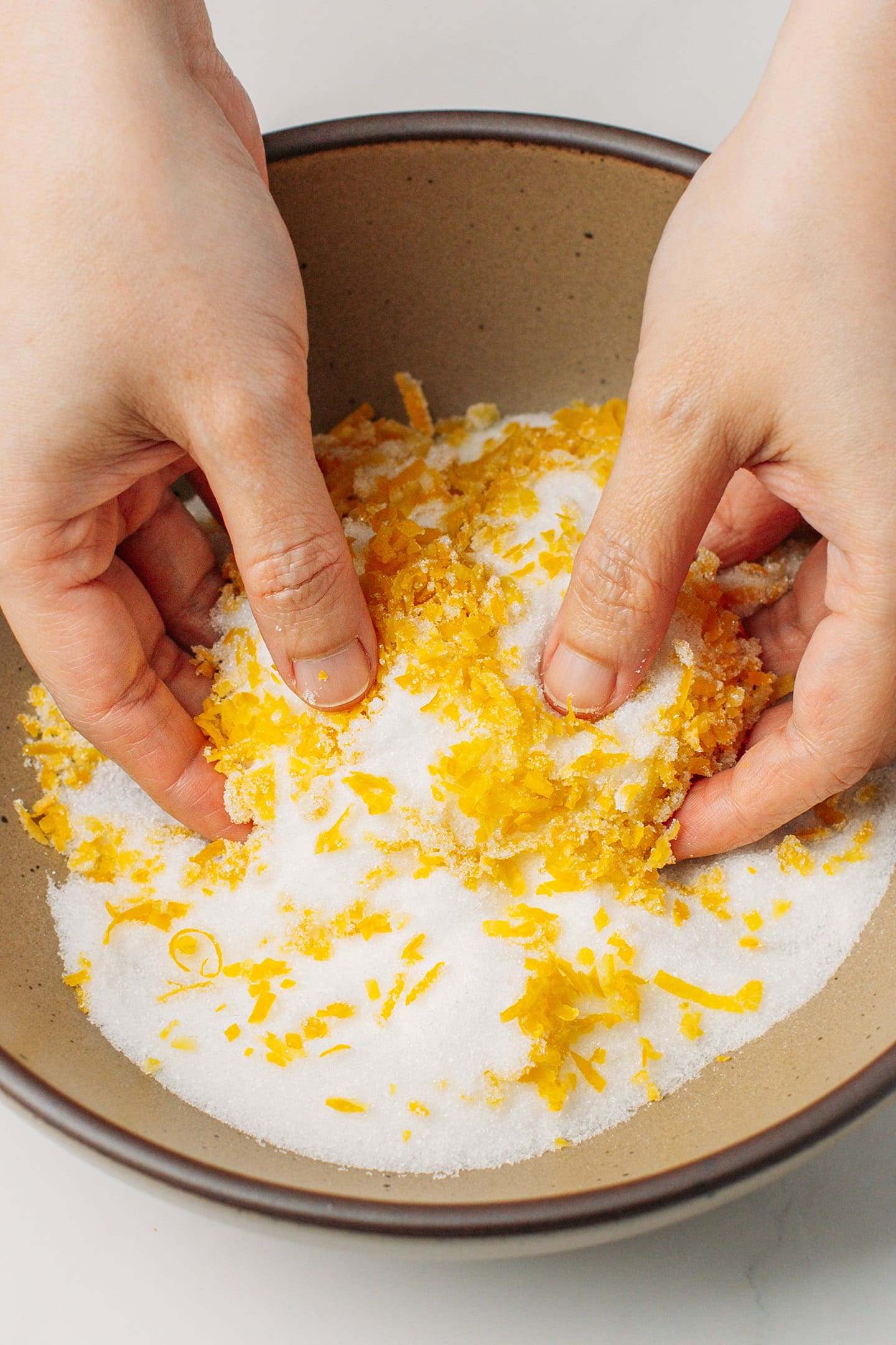 Rubbing lemon zest with sugar in a bowl.