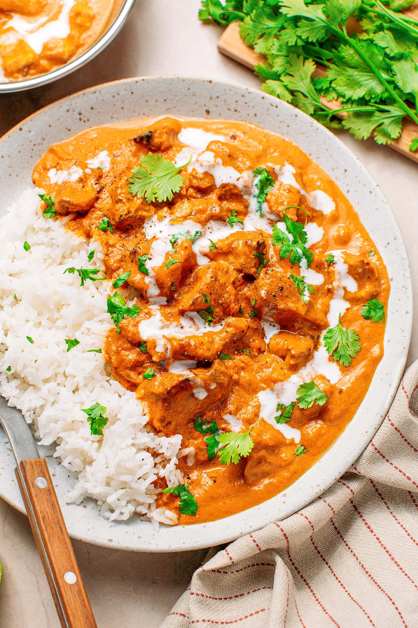 Close-up of creamy vegan butter chicken with rice and chopped cilantro in a plate.