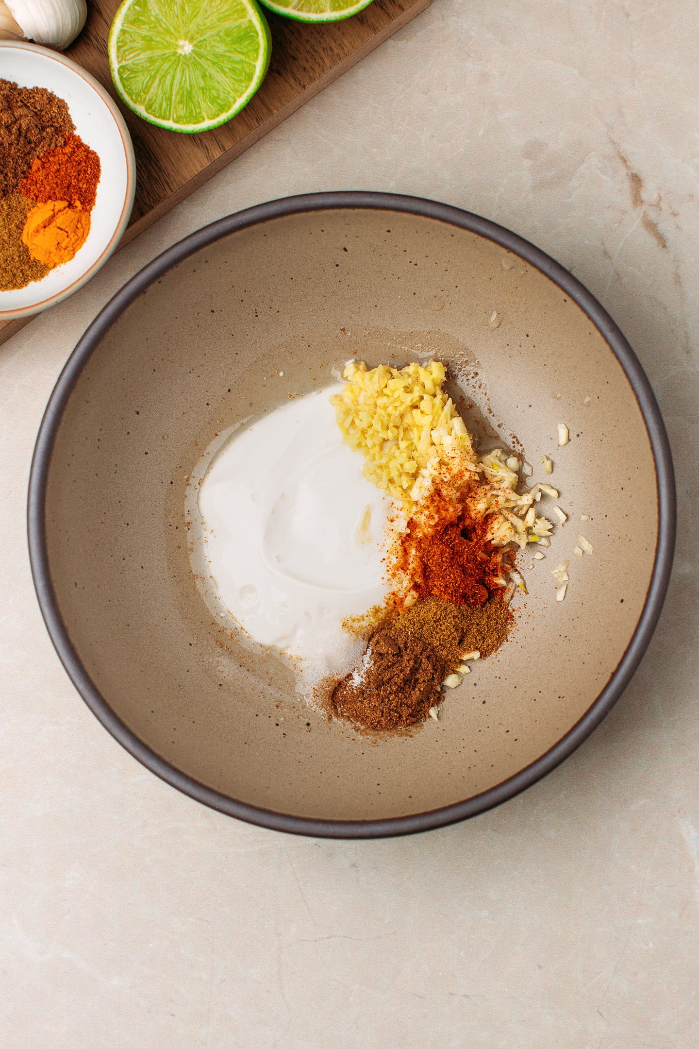 Yogurt, lime juice, spices, and chopped ginger in a bowl.